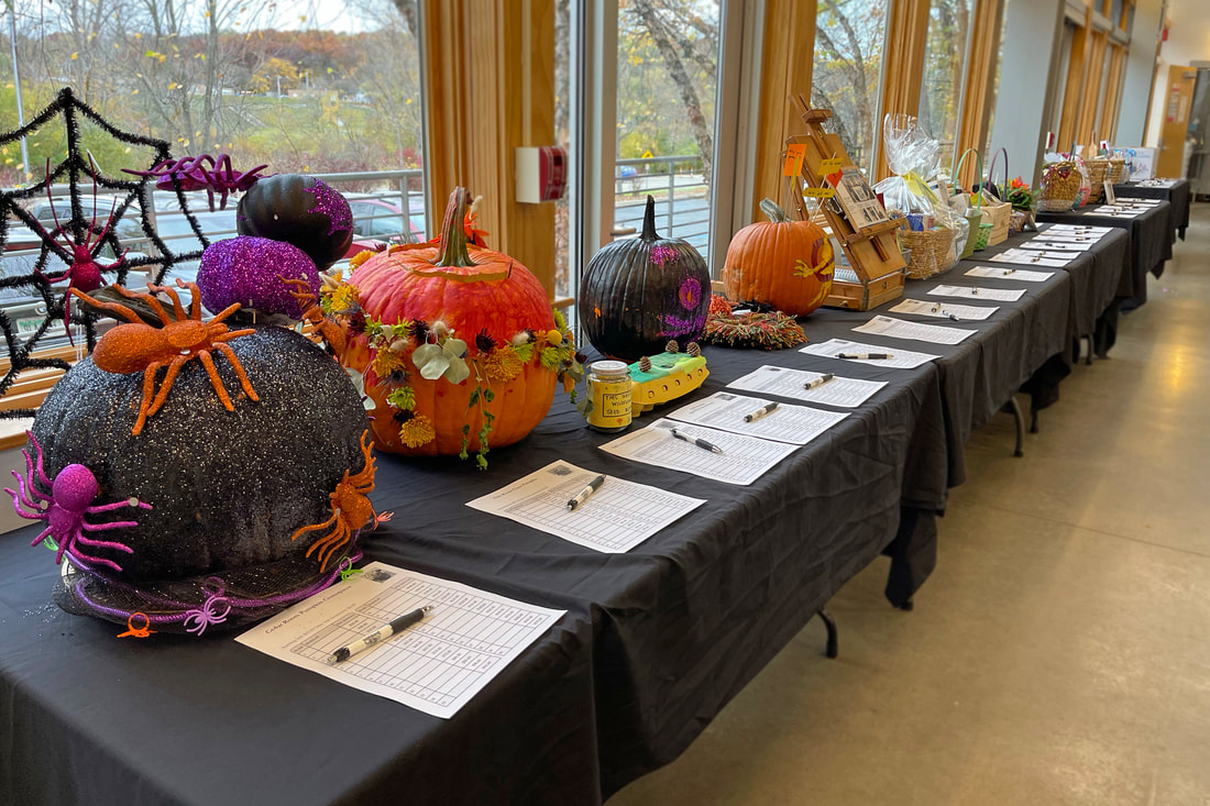 The silent auction tables featured at the 2022 Fall Festival event. Classroom decorated pumpkins are in the front with about 15 - 20 items after them.